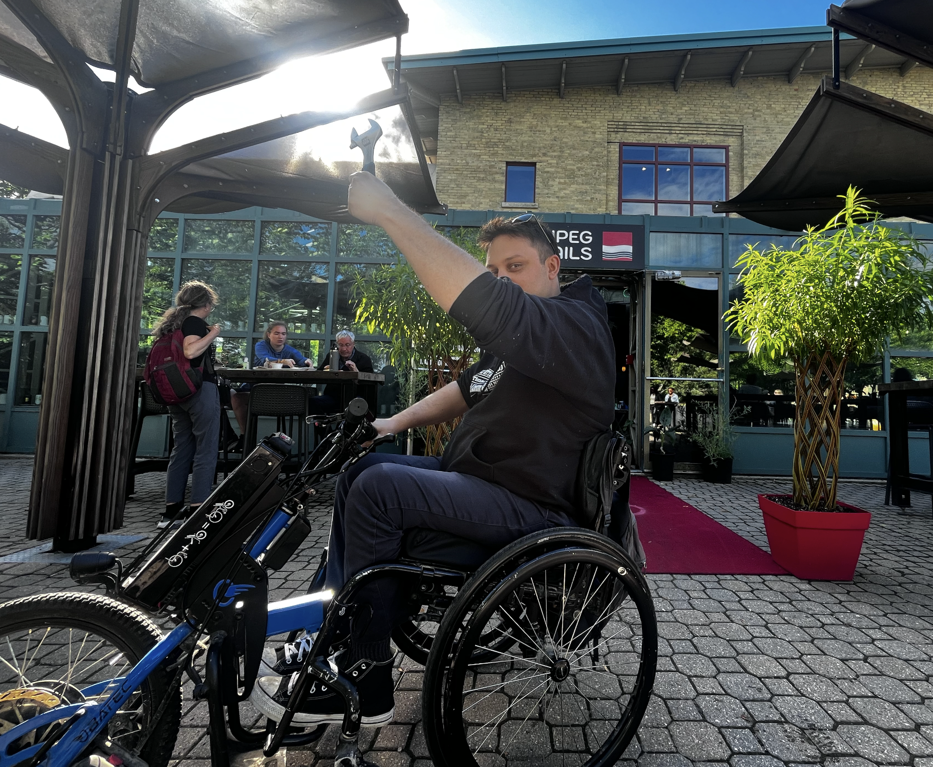 A golden hour photo, your event host, Peter, sitting in his wheelchair with its e-assist attached, holds a wrench up high to the sky catching the metallic glimmer