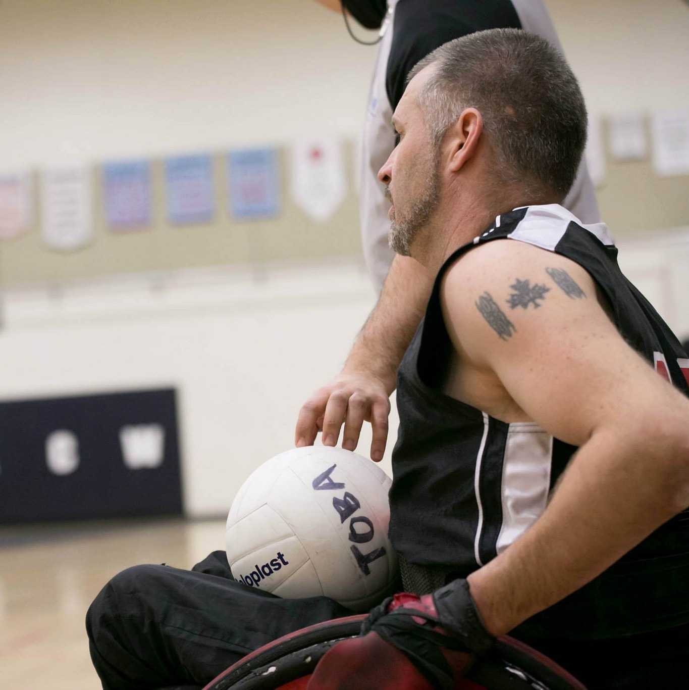 Jared funk in his team Canada jersey, rolls past the camera, a rugby ball in his lap, his Canada flag tattoo is prominent on his deltoid.